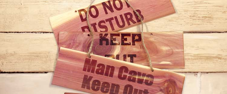 Wooden signs with messages DO NOT DISTURB, KEEP OUT, Man Cave, and KEEN OUT, hanging on ropes against a light wooden background.