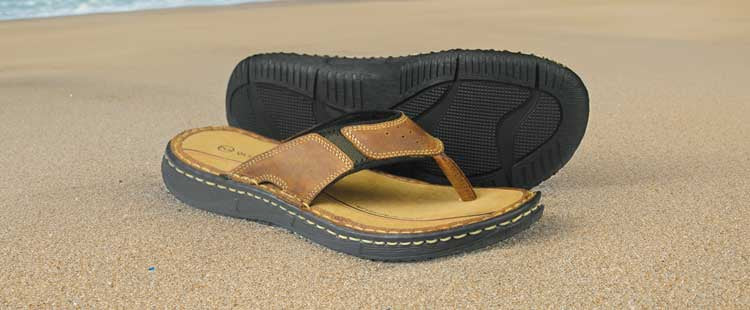 Go to the A pair of brown and black flip-flops with thick soles are placed on sandy beach with subtle waves in the background. collection