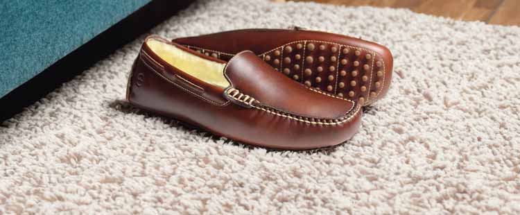 A pair of brown leather loafers with stitched detailing and rubber sole grips, placed casually on a textured beige carpet.