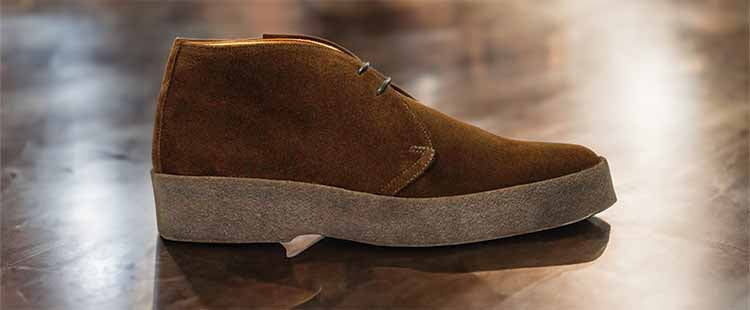 Go to the A brown suede chukka boot with light grey laces and a thick grey sole, placed on a reflective surface. collection