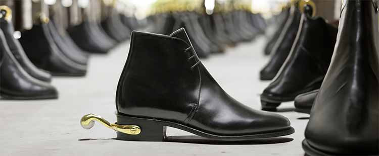 Go to the A row of shiny black leather boots is lined up on a smooth floor. Each boot features a distinctive gold spur at the heel, adding a unique touch to the classic design. collection