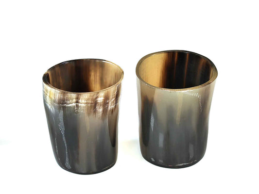 Two 3-inch tall shot glasses by Cathcart Elliot, crafted to mimic real horn with a smooth gradient of brown and black hues, evoke a Viking style with their glossy finish and uneven edges, standing elegantly against a plain white background.