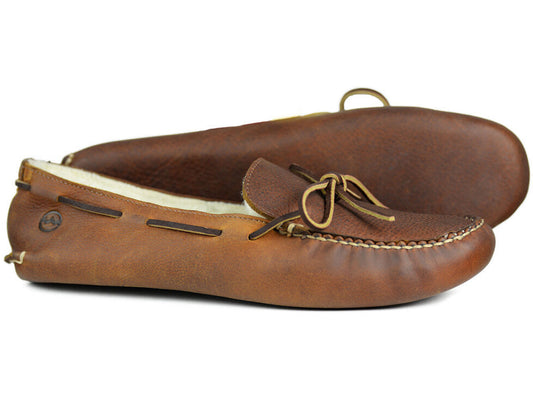 The SIOUX II Mens Slippers by Orca Bay are brown leather moccasins lined with genuine sheep fleece, featuring a tied lace design, visible stitching, and a soft, flexible sole. Displayed side by side on a white background.