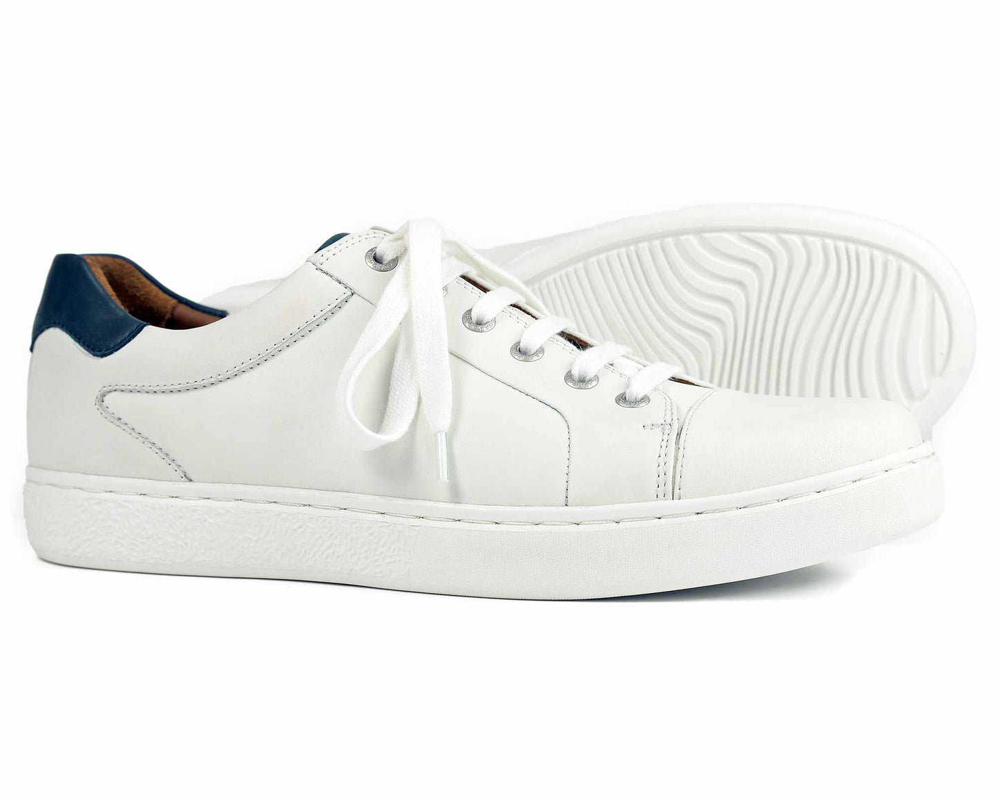 The Orca Bay Belgravia Mens White Sneaker features a navy heel trim, white leather design, and EVA rubber sole for comfort. Textured soles with white laces showcase lightweight design. One shoe stands upright while the other highlights the intricate sole pattern.