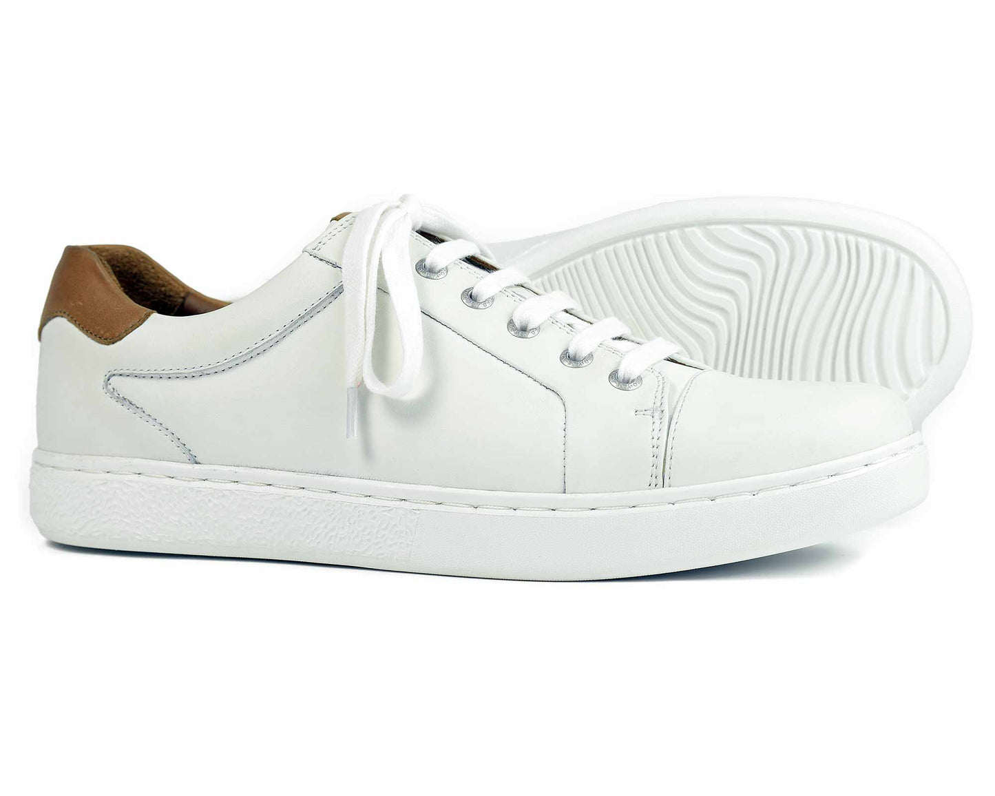 Orca Bays Belgravia Mens Sneaker features a sleek white leather design with tan accent heels, white laces, and thick soles. One shoe stands upright while the other lies on its side, highlighting the lightweight EVA rubber and grooved tread pattern.