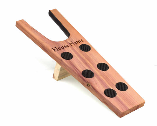 The 18mm thick Cathcart Elliot Personalised Cedar Wood Boot Jack features a U-shaped slot, textured footrest, black grips for traction, and rests on a supporting stand. Made from aromatic cedar wood, it is labeled House Name on the top.