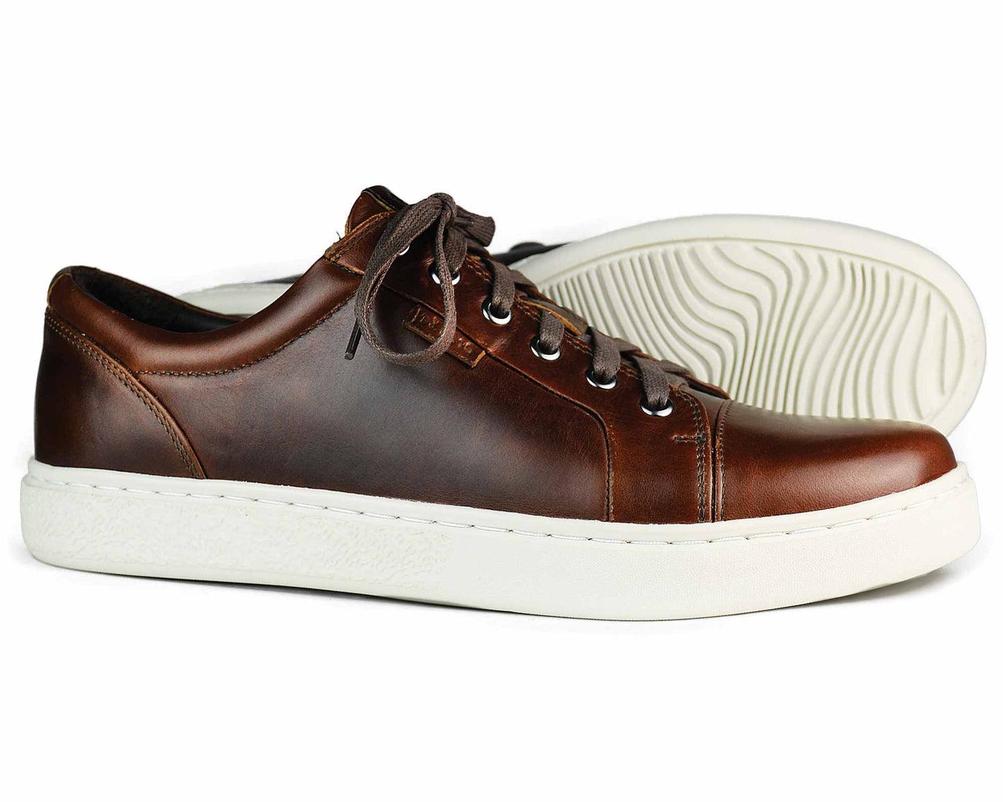 The KENSINGTON Mens Elk Brown Leather Sneaker by Orca Bay features brown laces, white rubber soles with a textured grip for style and function, and is an ideal lightweight summer shoe. One sneaker stands upright while the other lies on its side.