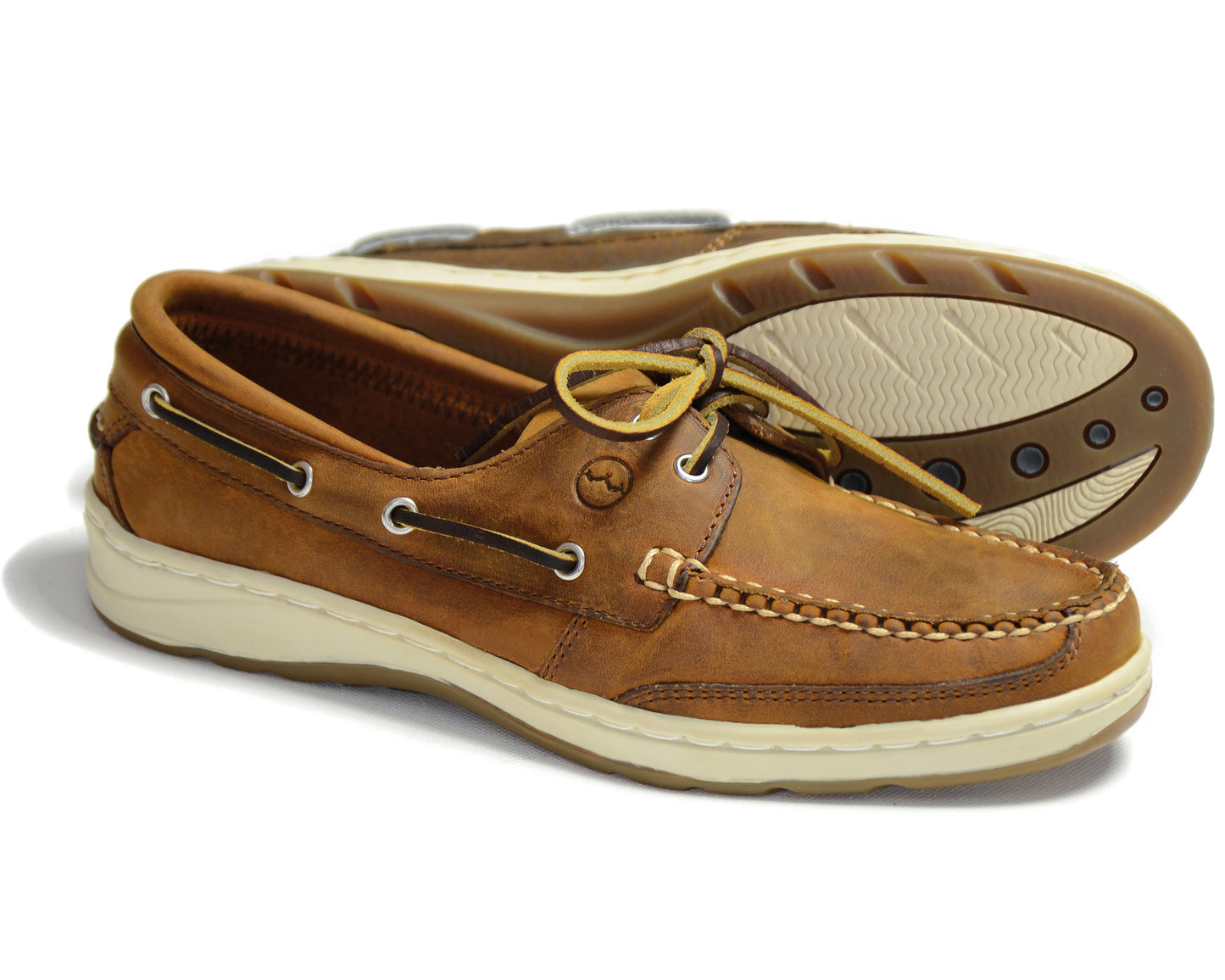 The LAGOON Ladies Sand Nubuck Boat Shoe by Orca Bay showcases brown laces threaded through side eyelets, white soles, and stitching details along the toe. One shoe stands upright while the other slightly tilts to reveal its sole.