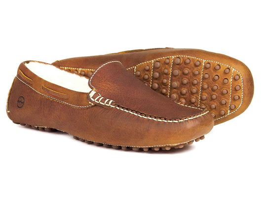 The MOHAWK II Havana Mens Real Sheep Fleece Lined Leather Slippers by Orca Bay are shown, featuring white stitching and rubber pebble soles. One slipper is sideways, highlighting the design, while the other displays its textured sole from the front.