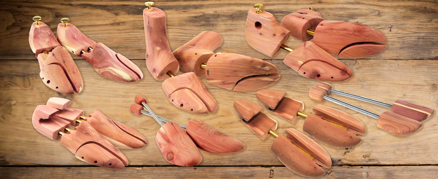 Various cedar shoe trees and stretchers are spread out on a wooden surface. The shoe trees are unfinished with brass hinges and knobs. The woods natural grain and reddish hue are visible.