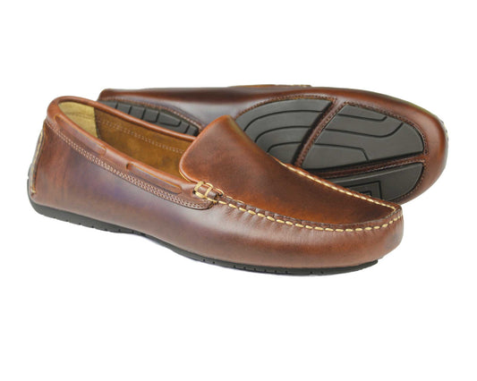 The SILVERSTONE Mens Brown Leather Driving Shoes by Orca Bay feature visible stitching and segmented rubber soles. One shoe is upright, displaying its side and top, while the other reveals the tread pattern. These lightweight loafers blend style with comfort in every step.